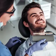 Dentystka dobiera odcień licówek kompozytowych dla uśmiechniętego pacjenta.