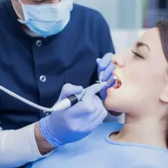 Dentysta bada zęby pacjentki. Zastanawiasz się, ile kosztuje wizyta u dentysty?