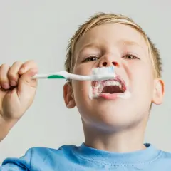 Chłopiec z pianą na ustach myje swoje mleczne zęby.