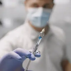 Dentysta w masce i rękawiczkach trzyma strzykawkę z płynem do znieczulenia nasiękowego.