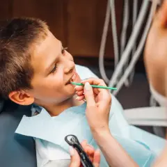 Chłopiec u dentysty, który bada jego zęby. Lekarz delikatnie dotyka jego dziąsła, sprawdzając, czy nie ma żadnej dziury w dziąśle.