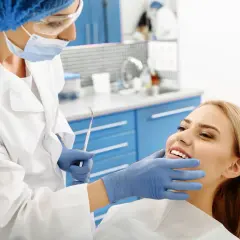 Dentysta bada uśmiechniętą pacjentkę, która może mieć nieleczone zapalenie okostnej zęba.