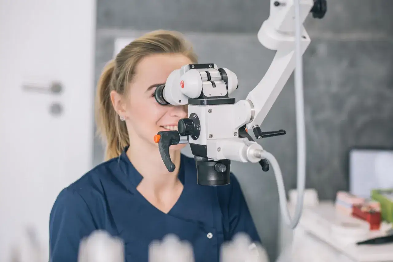 Dentystka z uśmiechem pracuje przy mikroskopie. Leczenie kanałowe pod mikroskopem cena jest dostępna w naszej klinice.