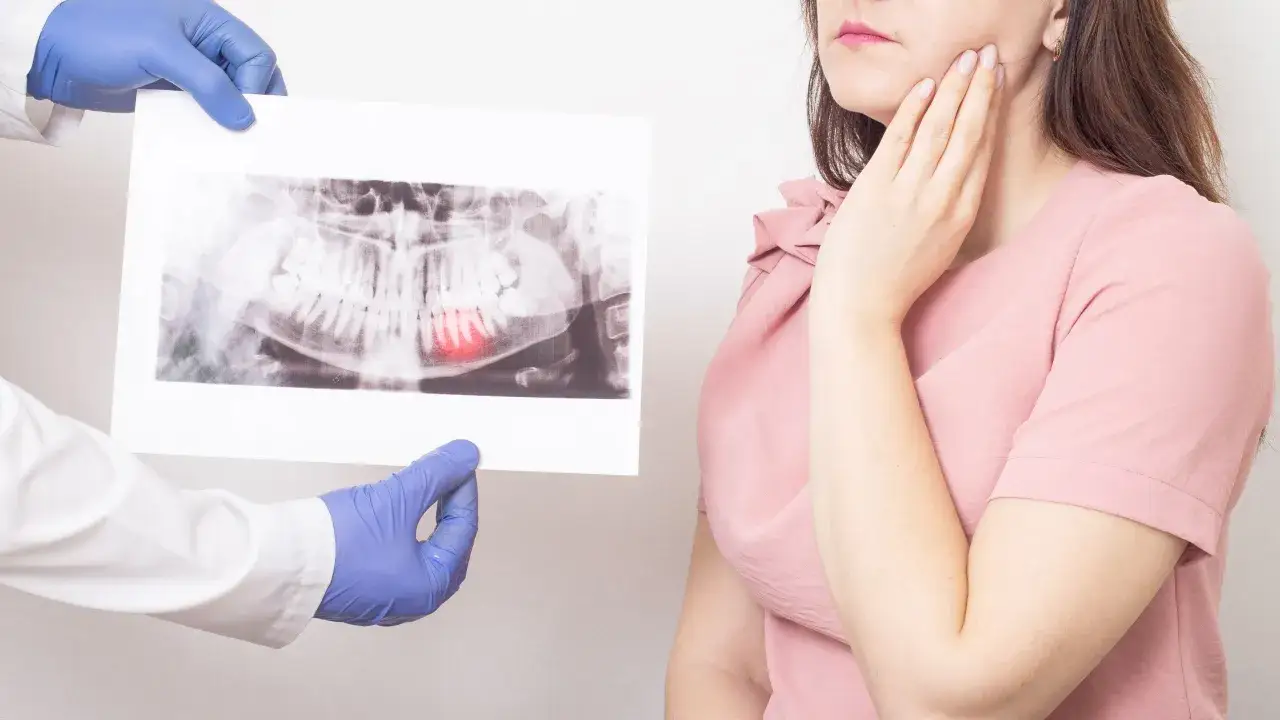 Dentysta pokazuje zdjęcie RTG z bolącym zębem, kobieta trzyma się za policzek.