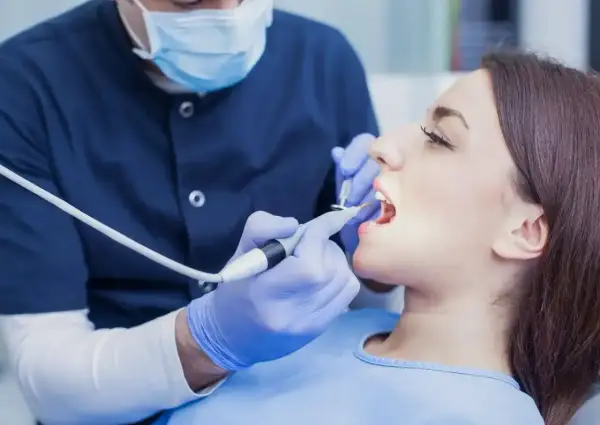 Dentysta bada zęby pacjentki. Zastanawiasz się, ile kosztuje wizyta u dentysty?