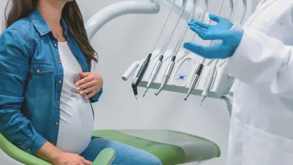 Ciężarna kobieta w gabinecie stomatologicznym, omawiająca leczenie kanałowe.