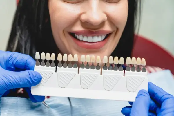 Uśmiechnięta kobieta z idealnymi zębami, dentysta dobiera odcień licówek ceramicznych.