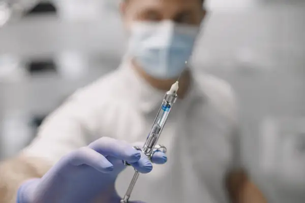 Dentysta w masce i rękawiczkach trzyma strzykawkę z płynem do znieczulenia nasiękowego.