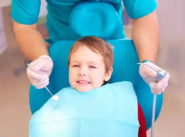Mały pacjent u dentysty, który szuka odpowiedzi: co na ból zęba u dziecka. Dentysta w rękawiczkach trzyma narzędzia.