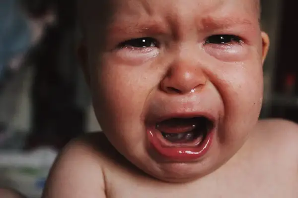 Malutkie dziecko płacze, ma zaczerwienione oczy i mokry nosek. To pewnie katar przy ząbkowaniu, który sprawia mu ból.