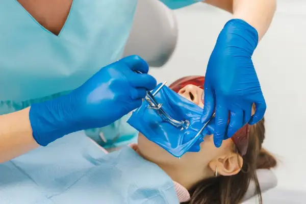 Dentysta zakłada koferdam pacjentowi, izolując pole zabiegowe.
